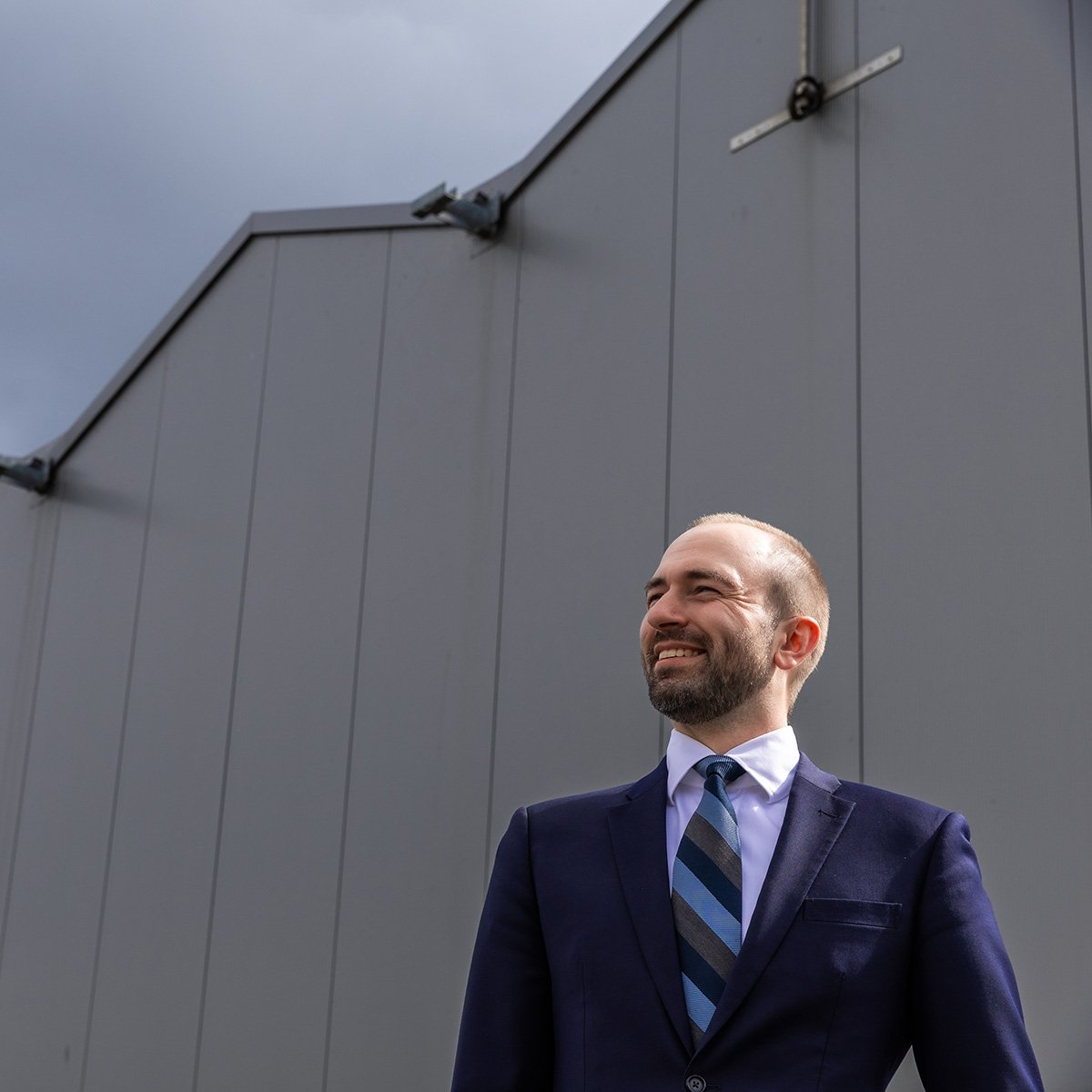 Aa person in a formal suit with a striped tie standing in front of a modern building with a white facade.