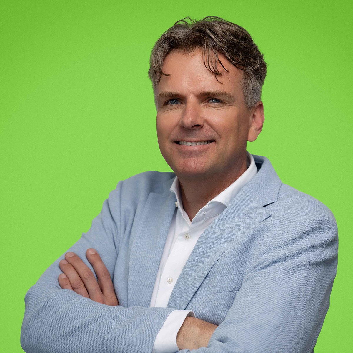A man in a blue suit with his arms crossed against a green background.