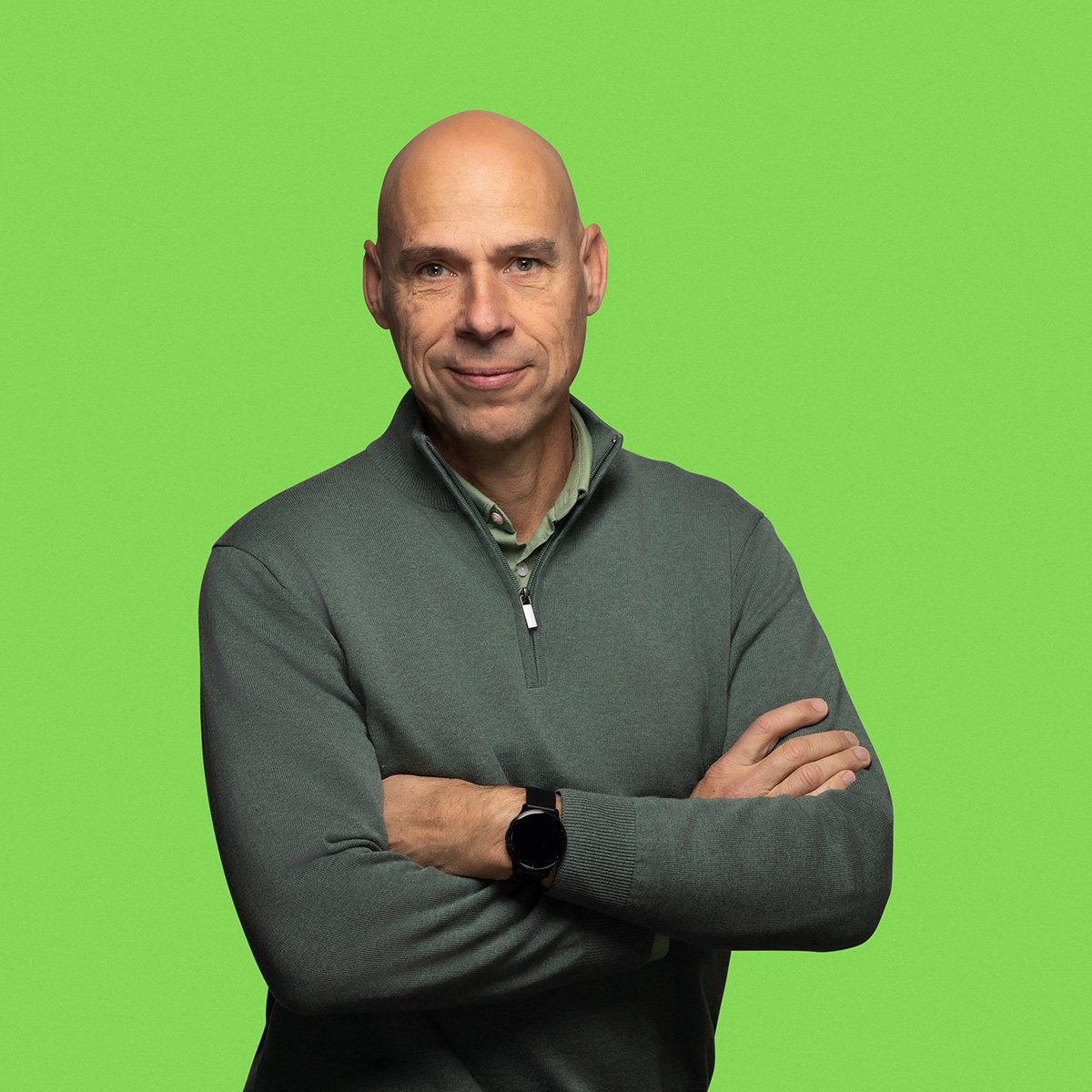 A person standing against a green background with their arms crossed.