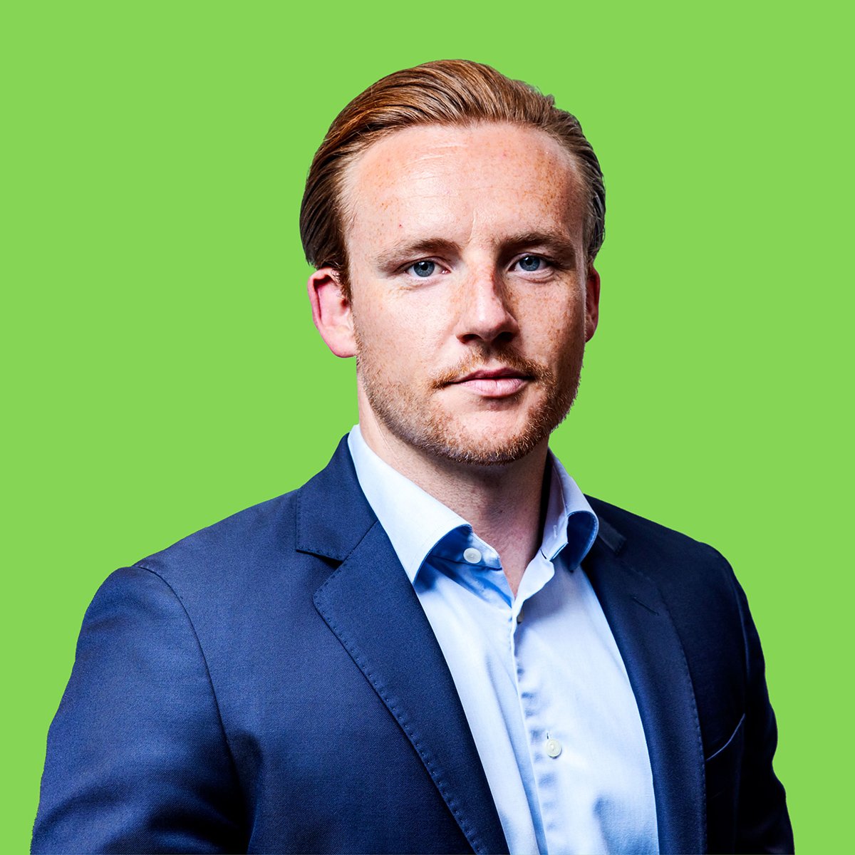The image shows a person wearing a blue suit jacket over a light blue shirt, set against a green background. The person's face is not visible.