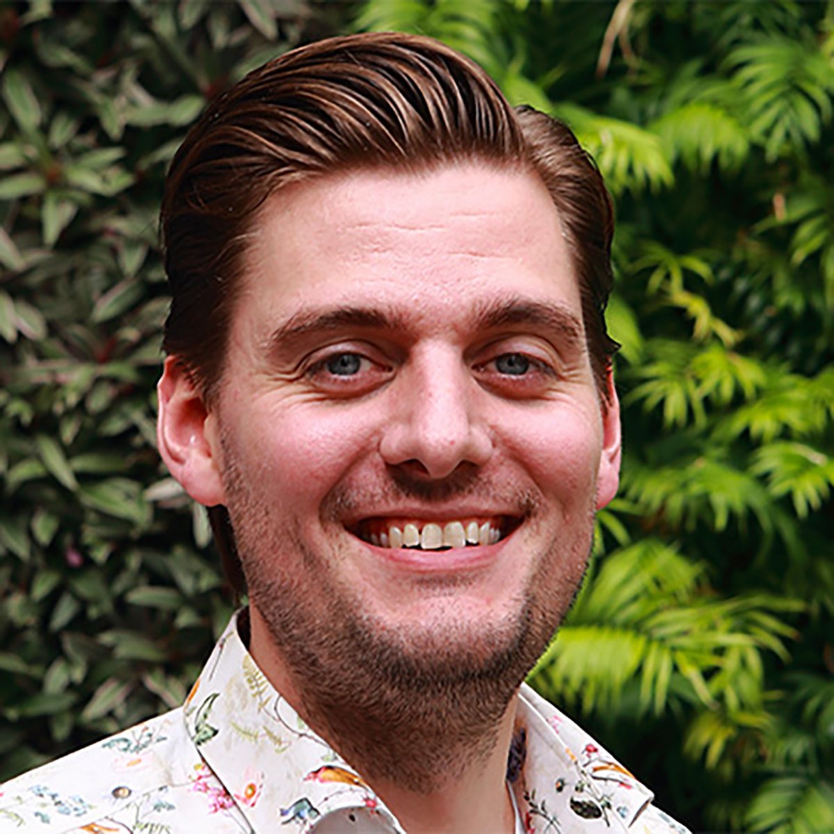 A person wearing a patterned shirt with a background of green foliage. The face is blurred and not described.