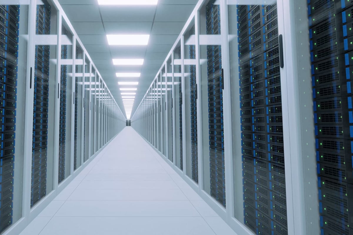 Een modern datacentrum met een reeks witte serverrekken die symmetrisch in een centrale gang zijn opgesteld. De gang wordt verlicht door felle plafondlampen en elk rek is uitgerust met talrijke computerservers, die allemaal verlicht worden door blauwe indicatielampjes.