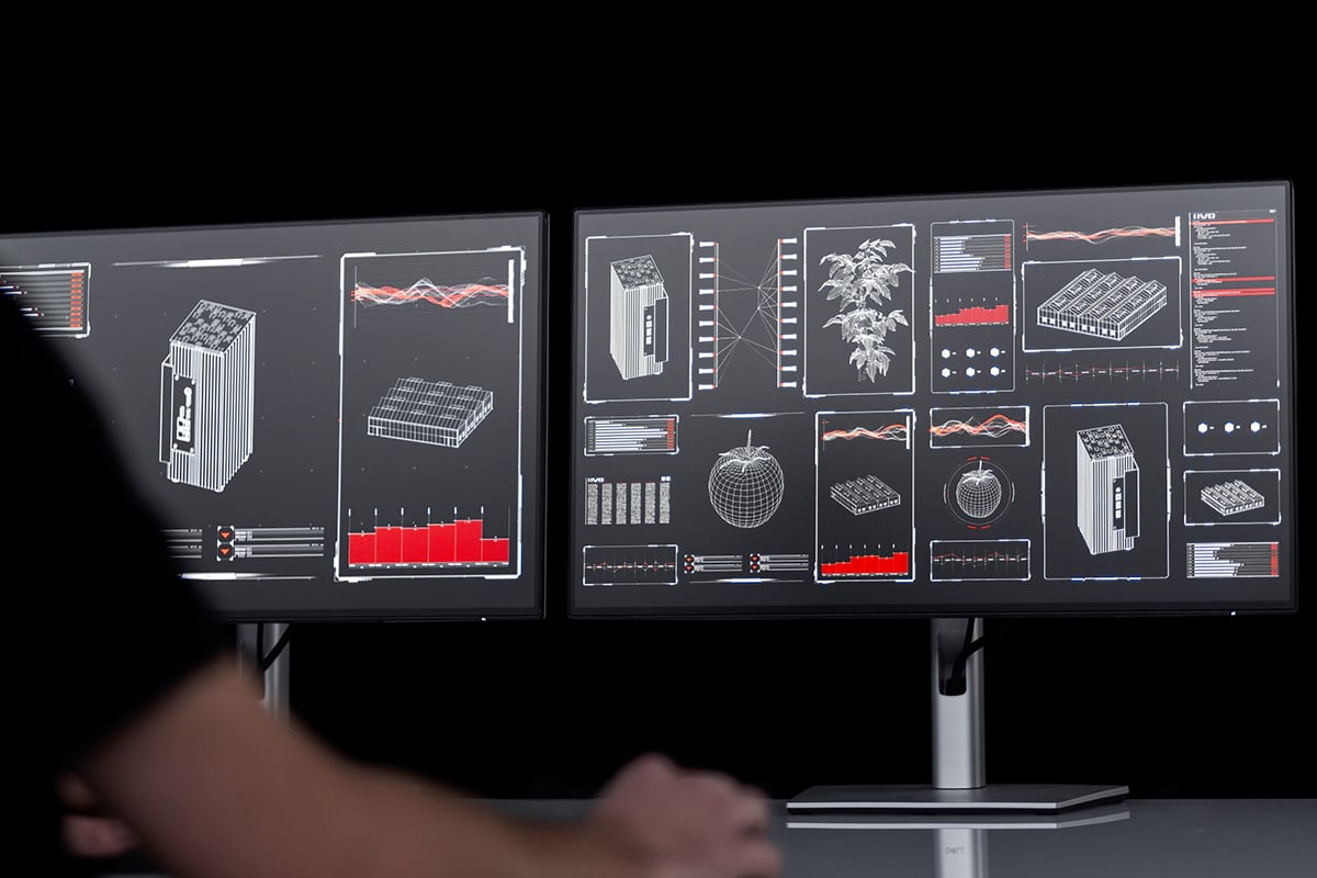 A person operating a large, multi-screen display system with various technical diagrams and data visualizations on each panel.