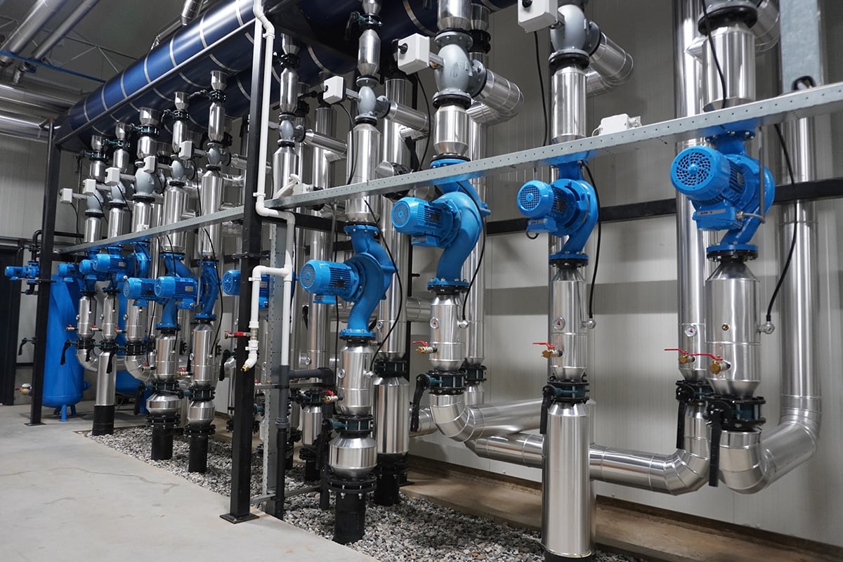 Een reeks industriële kleppen en pijpen, voornamelijk in blauwe en grijze tinten, geïnstalleerd op een schone en georganiseerde manier. De pijpen zijn verbonden met verschillende mechanische onderdelen, wat duidt op een systeem dat is ontworpen voor vloeistof- of gasverwerking.